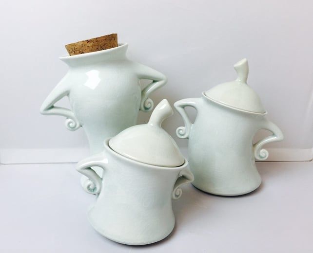 three white ceramic vases and a cork top are sitting side by side on a table