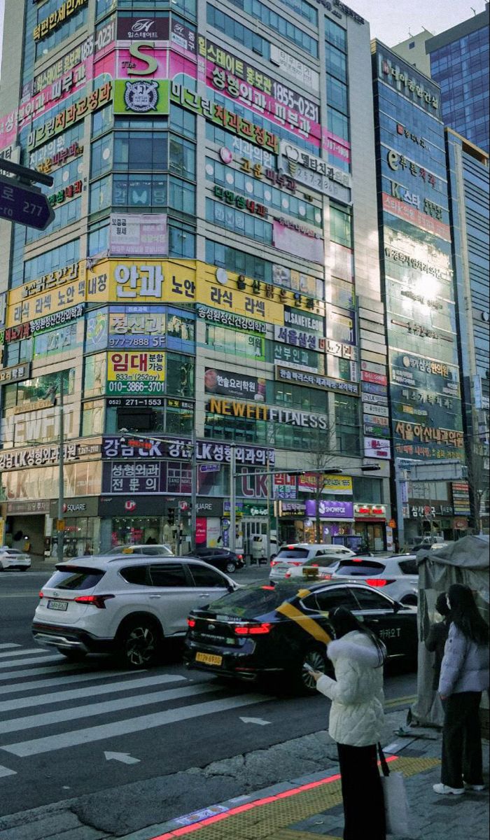 people are standing on the sidewalk in front of a tall building with many advertisements all over it