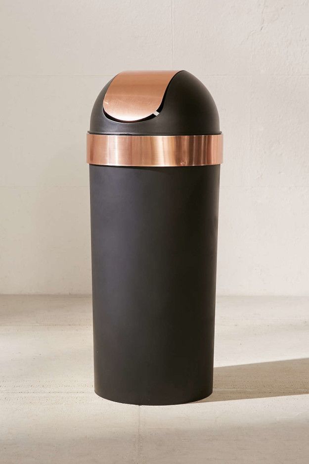 a black trash can with a rose gold top on the floor in front of a white wall