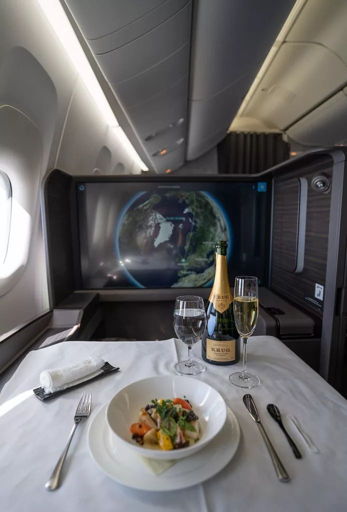 a plate of food and two wine glasses on an airplane seat with the television in the background