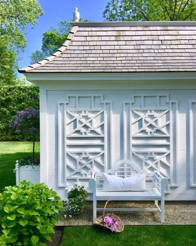 a white bench sitting in the grass next to a small building with lattice design on it