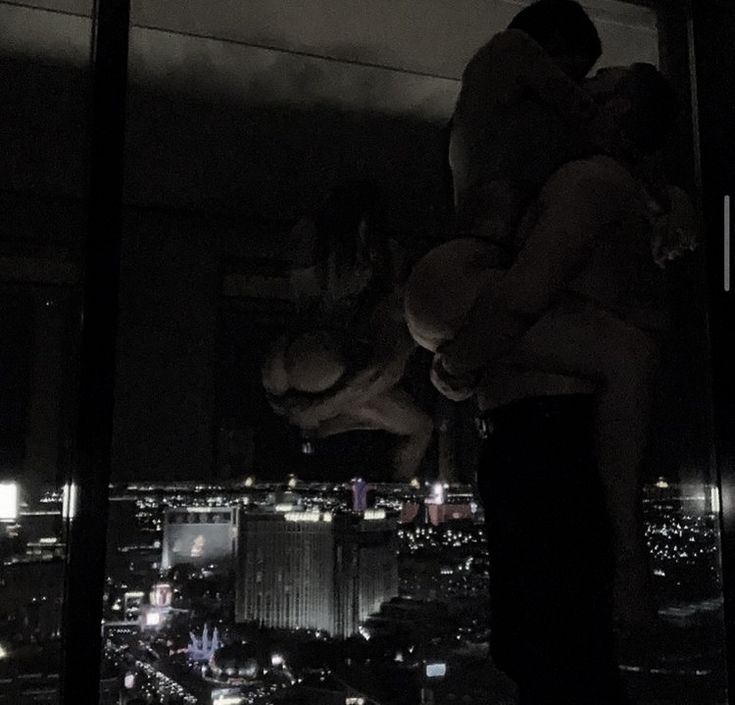 two men and a woman standing in front of a window with the city lights behind them