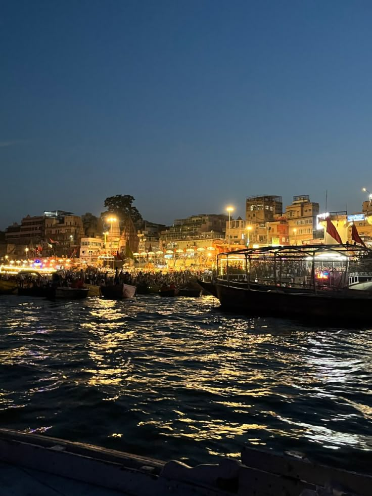 the boats are docked in the harbor by the city at night time, with lights on