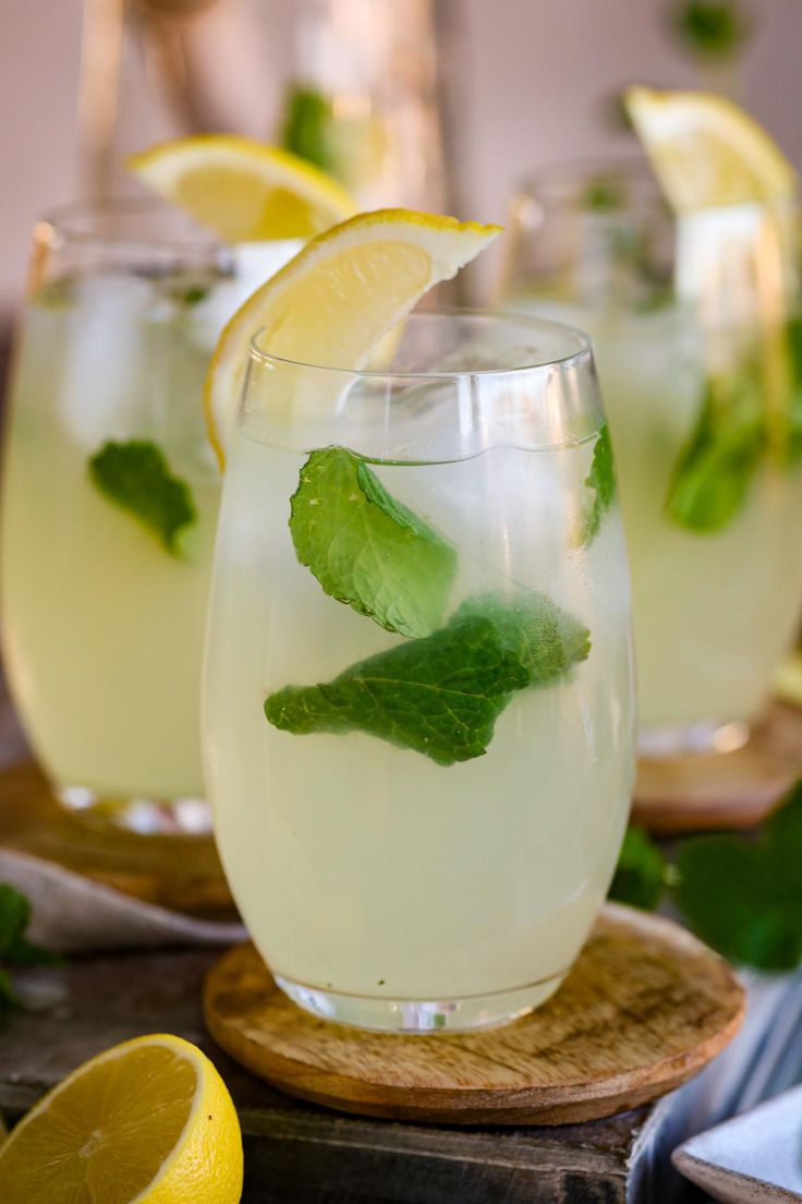 two glasses filled with lemonade and mint garnish on a cutting board next to sliced lemons