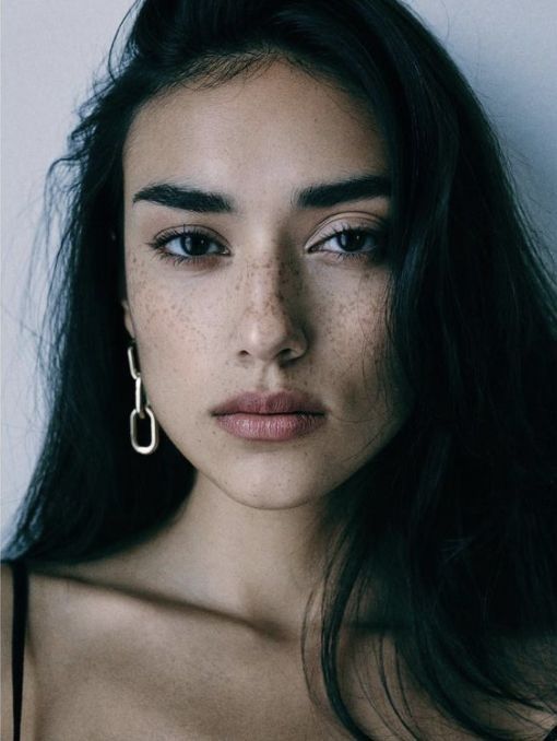 a woman with freckles on her face is posing for a photo in front of a white wall