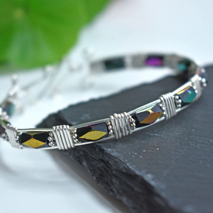 a close up of a silver bracelet on a black rock with a green leaf in the background