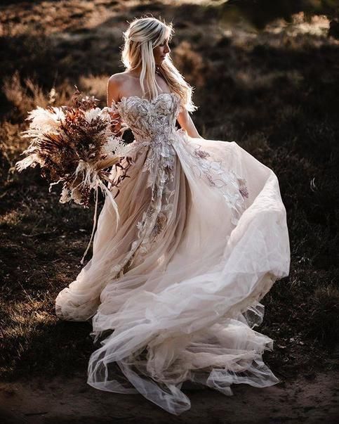 a woman in a wedding dress is walking through the grass with her hair pulled back