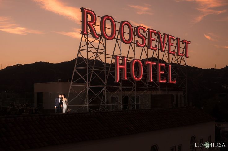 a couple standing on top of a roof next to a neon sign that reads rooseweel hotel