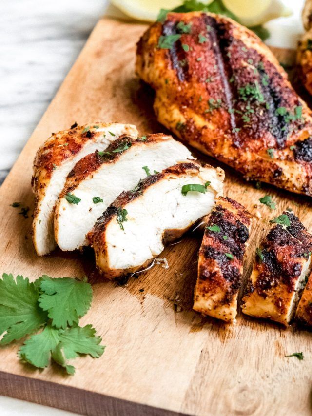 grilled chicken on a cutting board with parsley and lemon wedges next to it