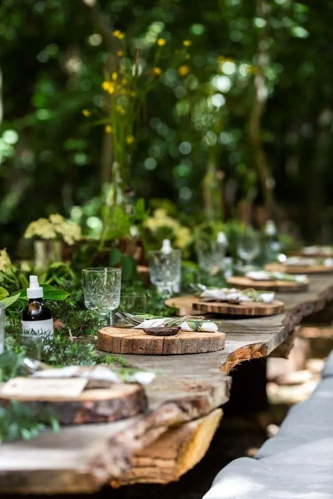 a long table with plates and glasses on it in the middle of a forest filled with trees