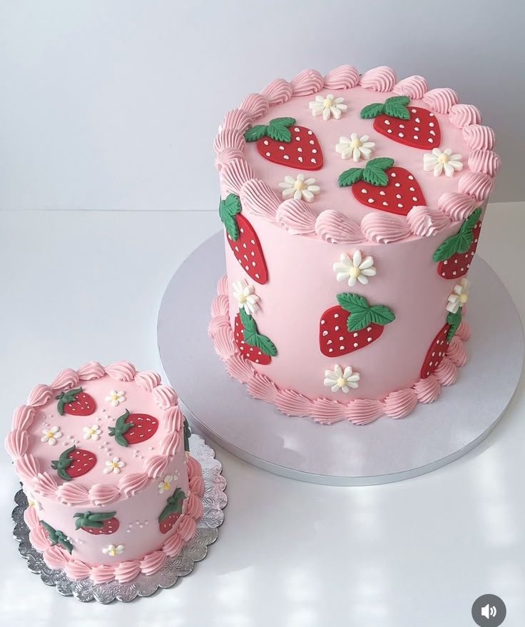 there is a pink cake with strawberries on it and two small cakes next to it