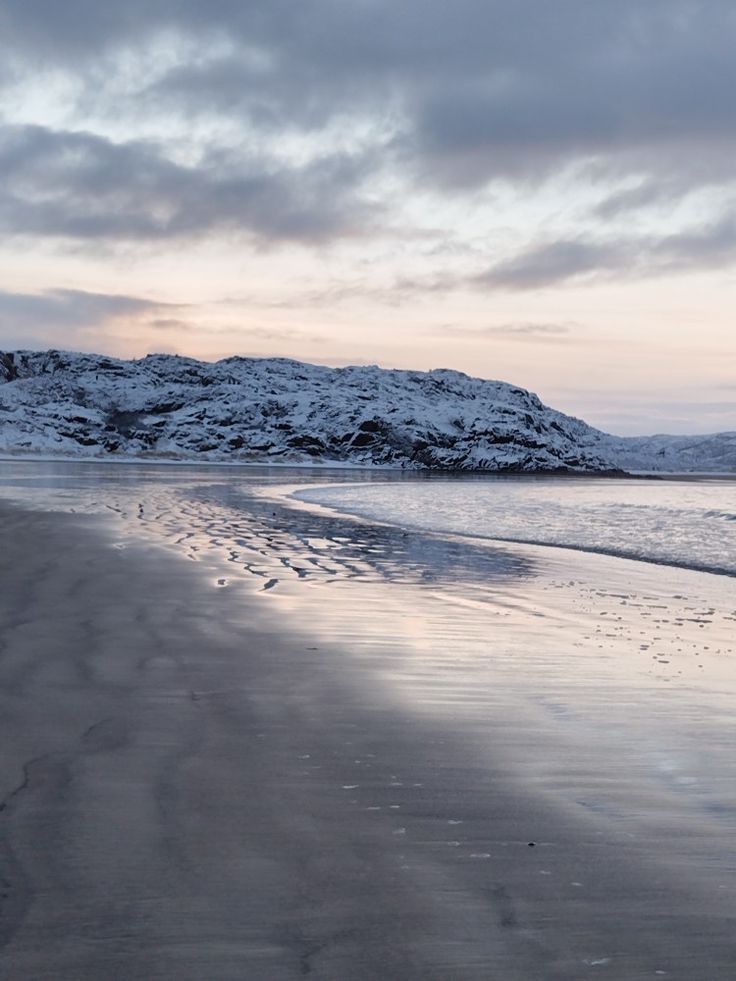 the beach is covered in snow and has footprints coming out of the sand to the water