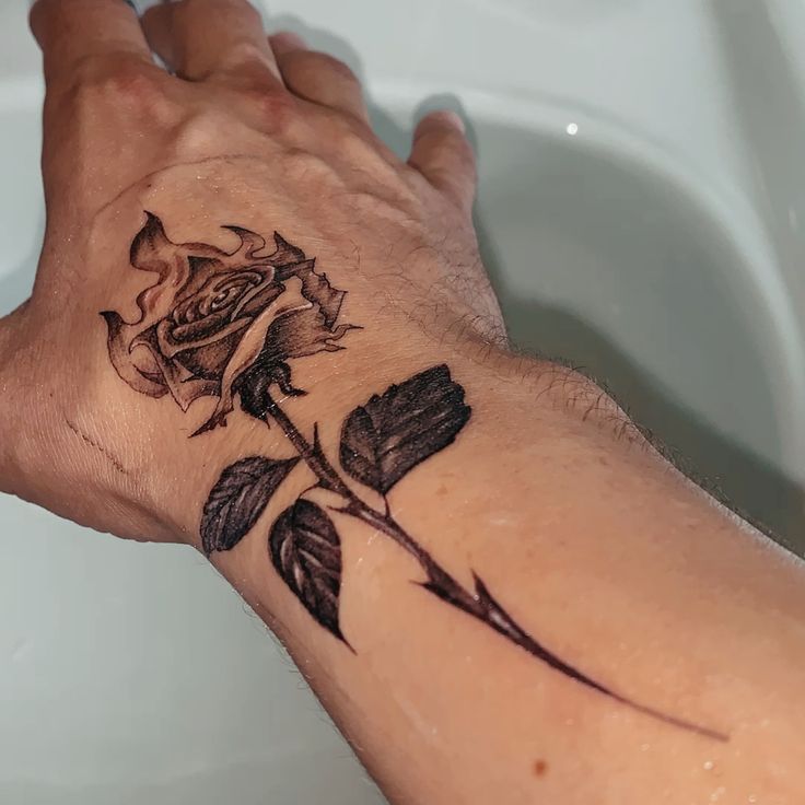 a person's hand with a rose tattoo on the left side of their arm