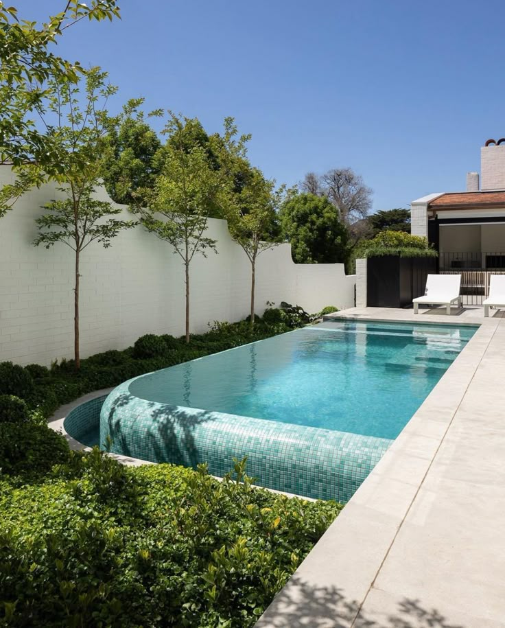 an empty swimming pool surrounded by greenery and trees in front of a white fence