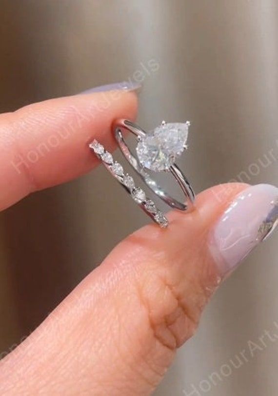 a woman's hand holding an engagement ring with two diamonds on the top and bottom