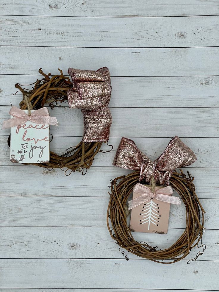 two wreaths with ribbons and tags hanging on the side of a white wooden wall