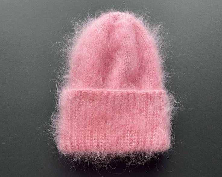 a pink knitted beanie sitting on top of a black table next to a pair of scissors