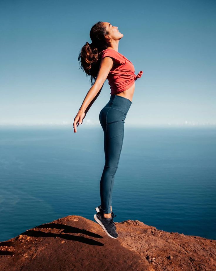 a woman standing on top of a rock next to the ocean with her arms in the air