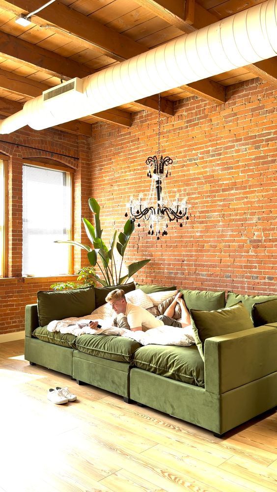 a green couch sitting in front of a brick wall with a chandelier hanging from the ceiling