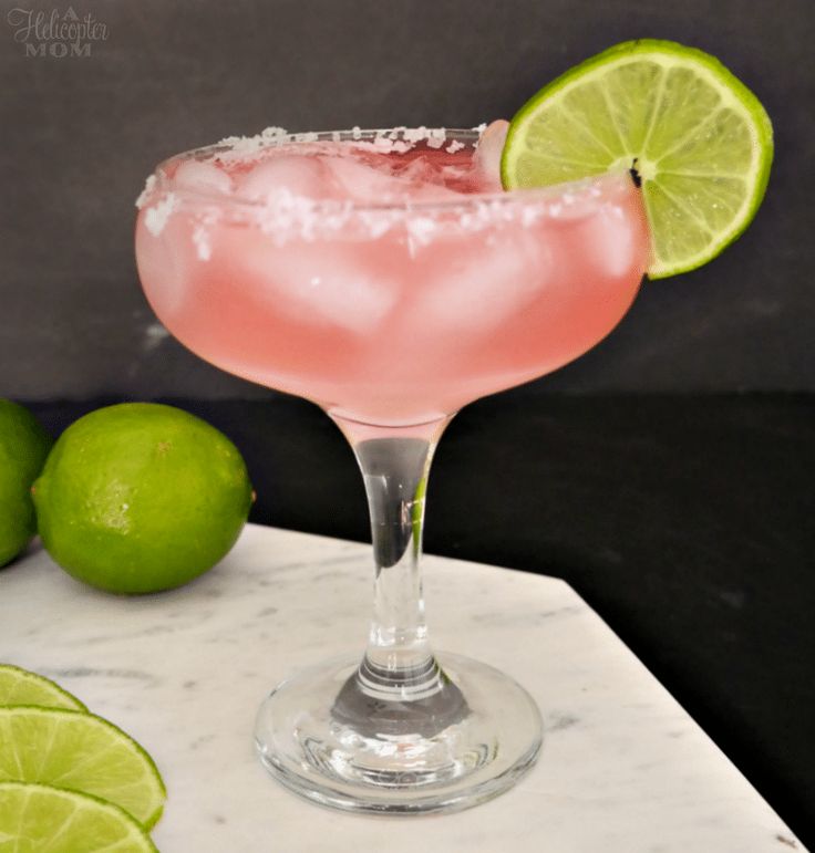 a pink margarita with limes and salt on the rim in front of a marble table