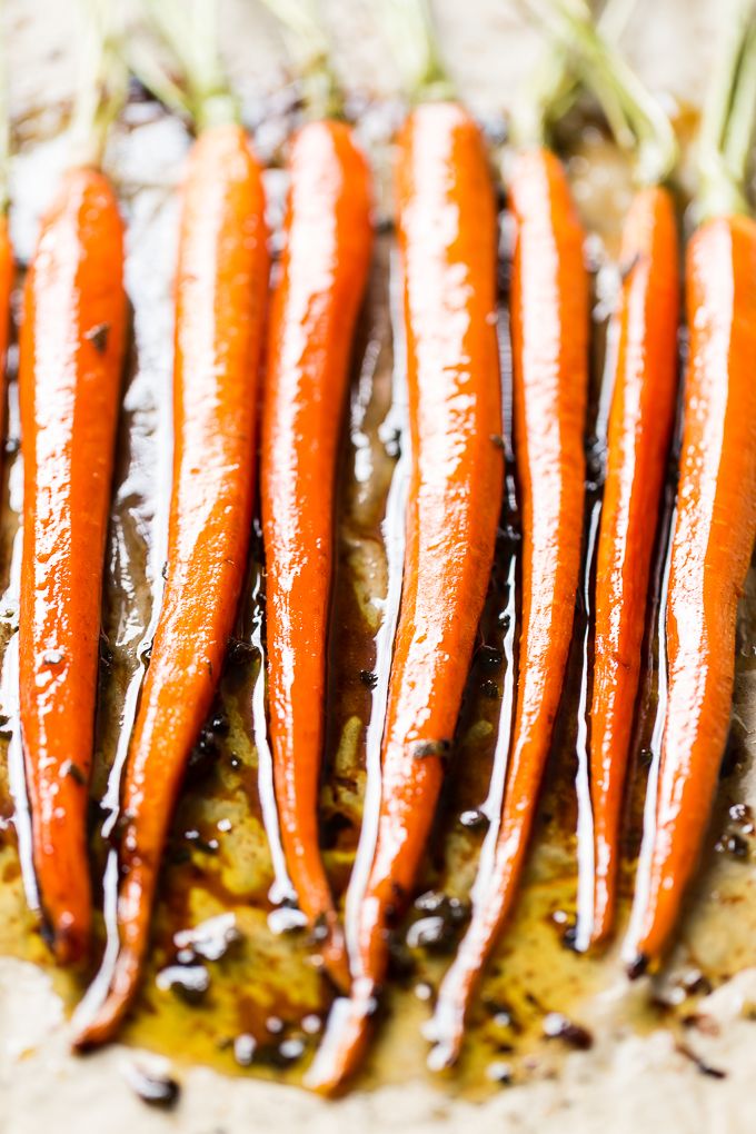 four carrots are being drizzled with brown sauce on a baking sheet