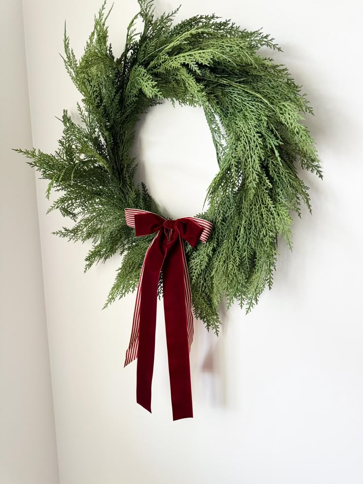 a green wreath with red ribbon hanging on the wall