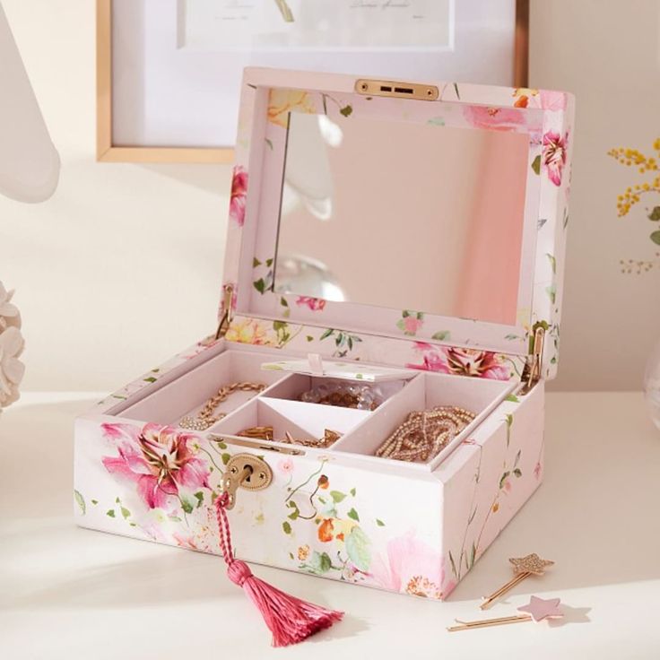 an open pink floral jewelry box sitting on a table next to flowers and other decorations