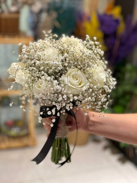 a bouquet of white roses is held by a woman's hand in a flower shop