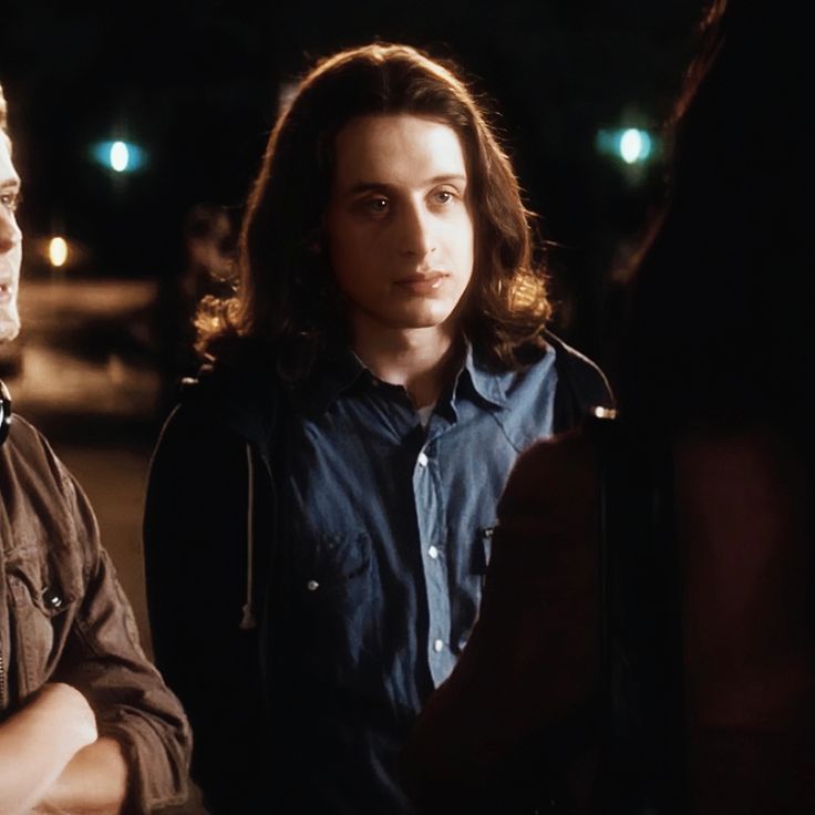 two young men standing next to each other in the street at night, one is looking off into the distance