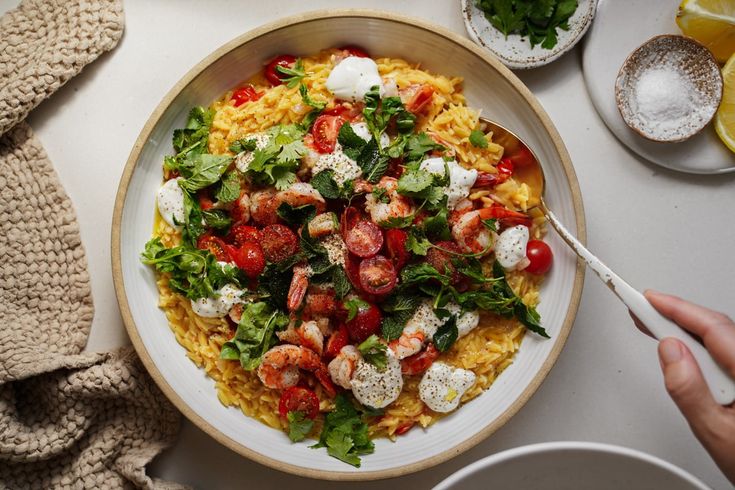 a plate of pasta with shrimp, tomatoes and feta cheese on it next to a cup of coffee