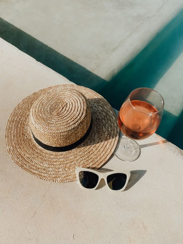 a straw hat, sunglasses and a glass of wine sit on the edge of a pool