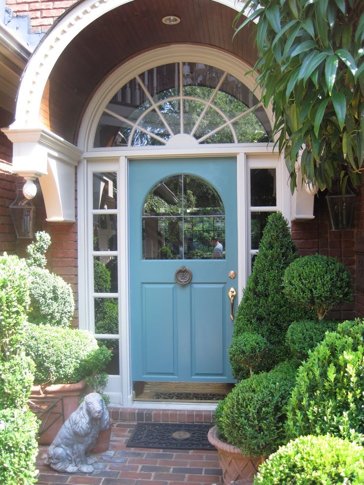 a blue front door surrounded by potted plants and bushes with a dog statue in the foreground