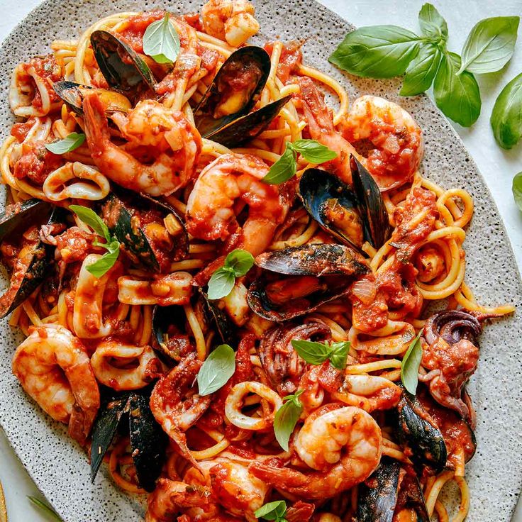 pasta with clams, mussels and sauce on a plate next to basil leaves