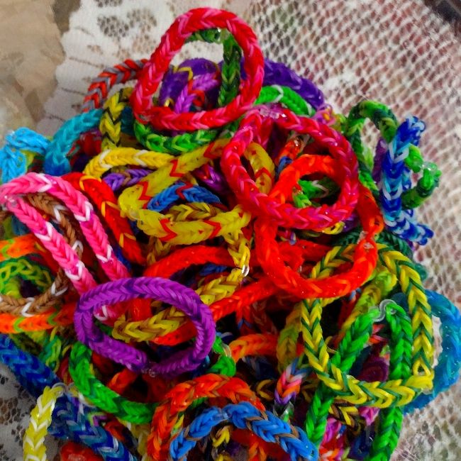 a pile of colorful bracelets sitting on top of a lace covered tablecloth next to a cup