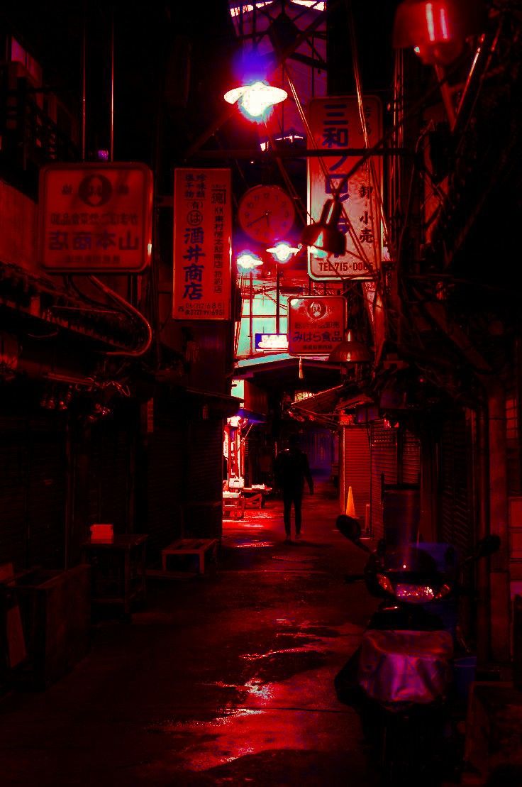 a person walking down a dark alley way at night with neon signs on the buildings