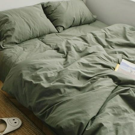 an unmade bed with green sheets and pillows on the floor next to a pair of slippers