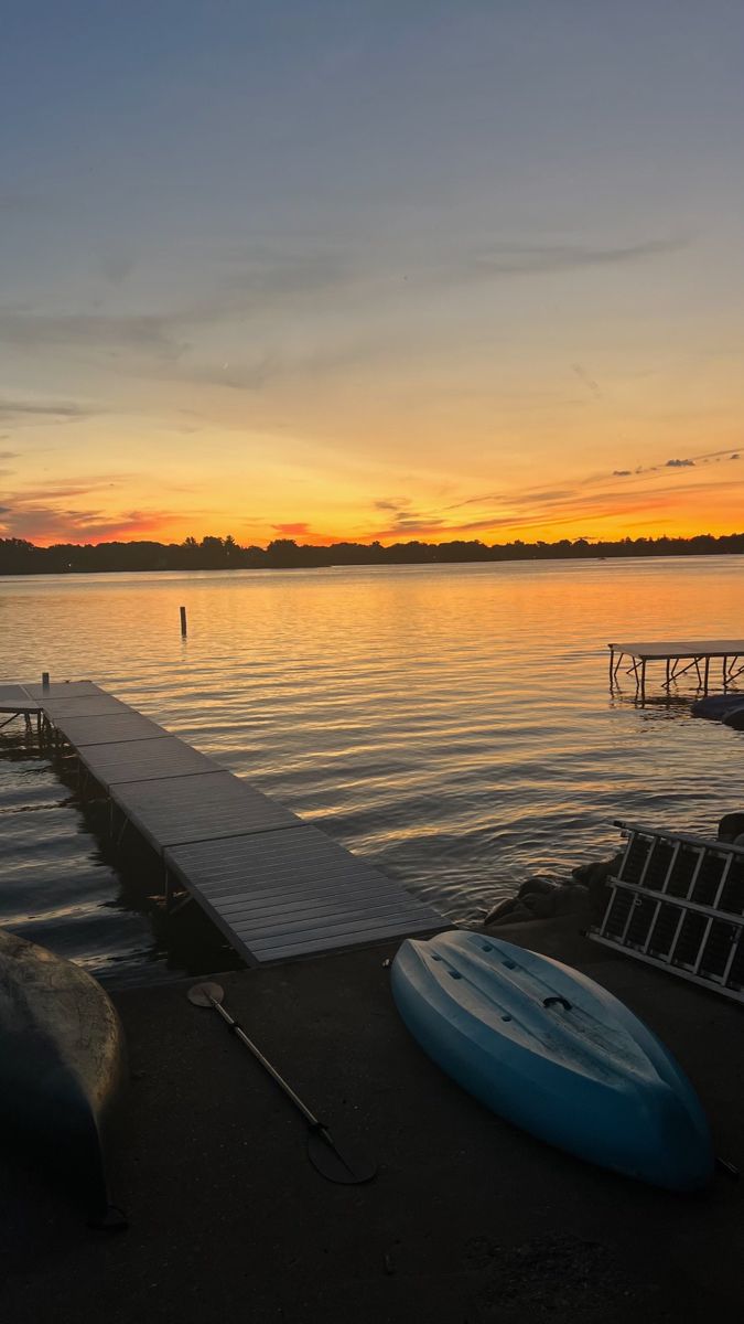 the sun is setting over the water and there are two surfboards on the dock