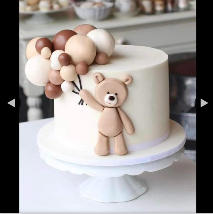 a teddy bear holding balloons on top of a white cake