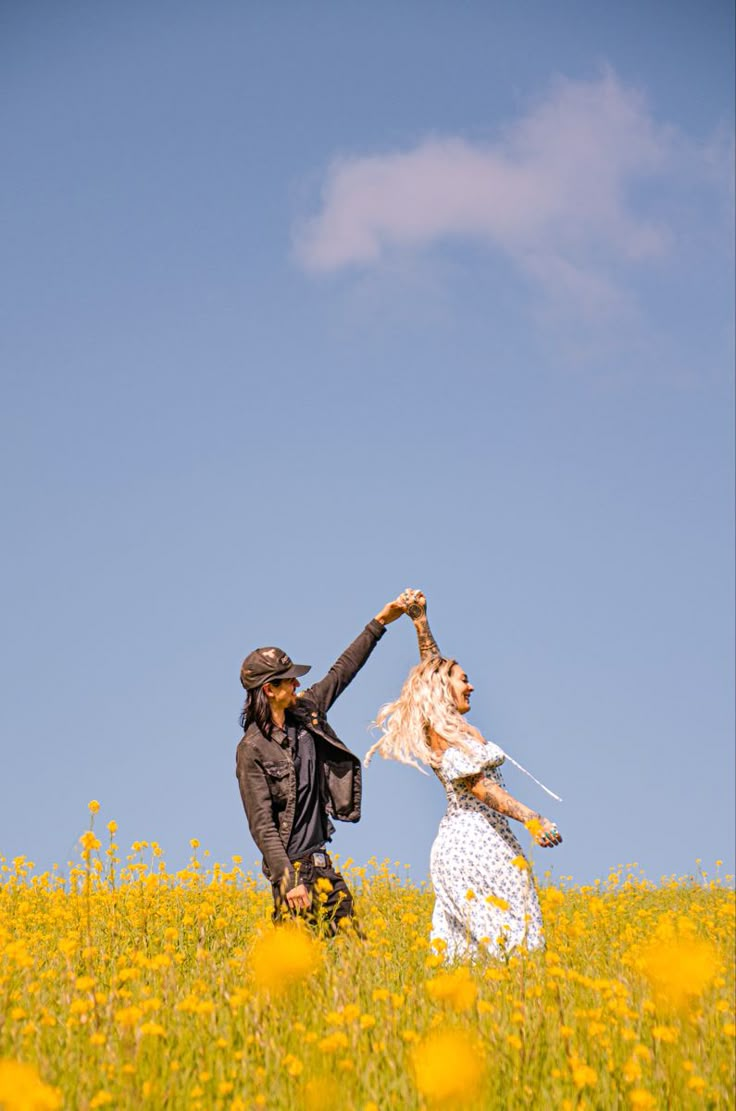 a man and woman are in a field with yellow flowers holding each other's hands