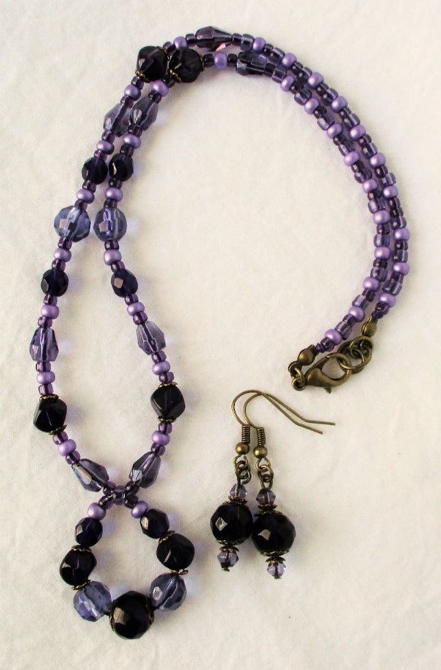 Purple Beaded Necklace Necklace: 18" in length, made with glass beads and seed beads in purple, brass layered bead caps and lobster clasp, adjustable to 18.5", strung on purple beading cord, perfect for collared blouses or crew neckline. Earrings: 1.5" in length, made with glass beads, brass accents, and ear hooks. This Purple Beaded Necklace will ship to you in a gift box, securely mailed in a padded envelope. Shipping same or next day, thru USPS Ground Advantage, tracking and insurance include Purple Beaded Necklace With Round Black Beads, Adjustable Lavender Beaded Necklaces, Adjustable Purple Beaded Necklace With Dangling Beads, Purple Czech Glass Beads For Jewelry Making, Purple Beaded Necklace With Black Beads For Gift, Purple Necklace With Black Beads, Handmade Czech Glass Purple Beads, Adjustable Purple Necklaces With Dangling Beads, Adjustable Purple Necklace With Dangling Beads