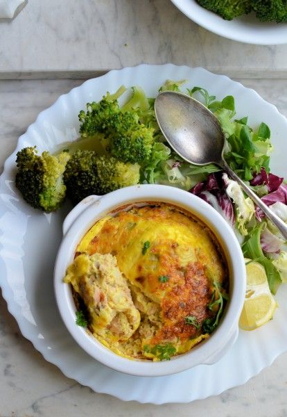 a white plate topped with a bowl of food next to a pile of broccoli