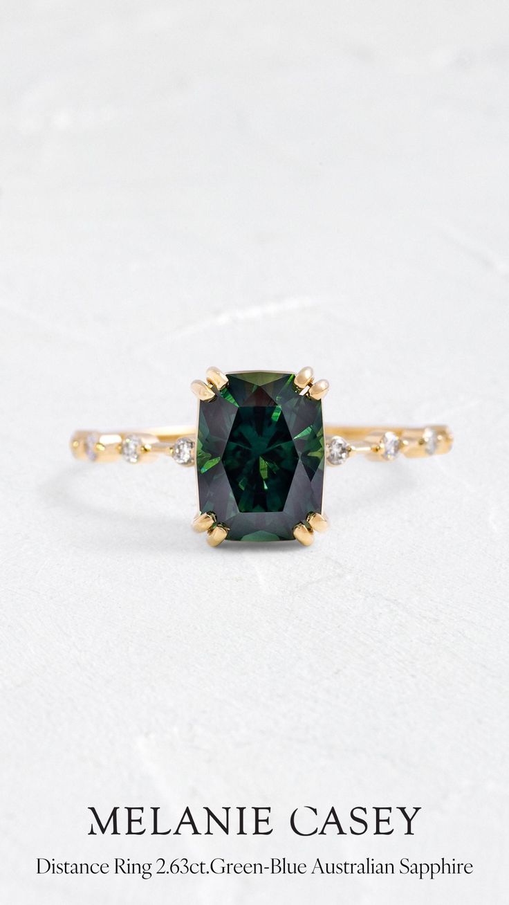 an emerald colored ring with diamonds on the band and side stones in yellow gold plated silver