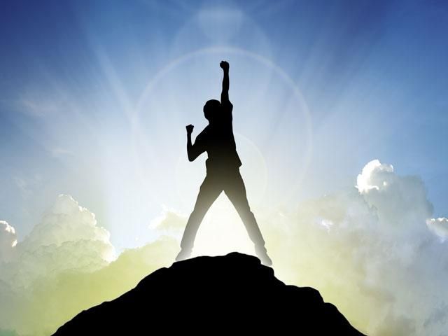 a person standing on top of a mountain raising their arms in the air with clouds behind them