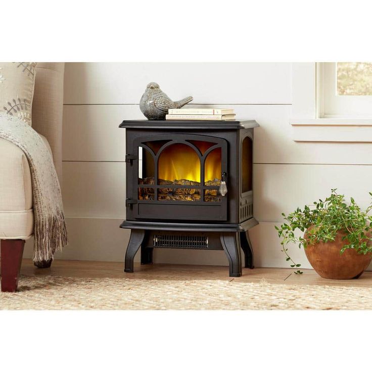 a black stove with a fire in it next to a potted plant on the floor