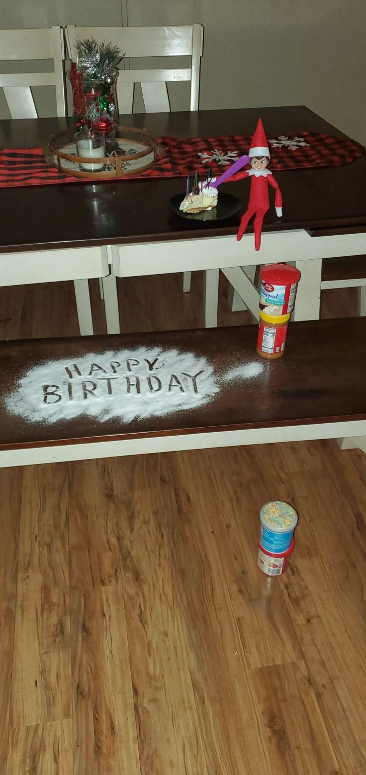 a birthday cake is on the table with an elf figure next to it and a bucket of paint