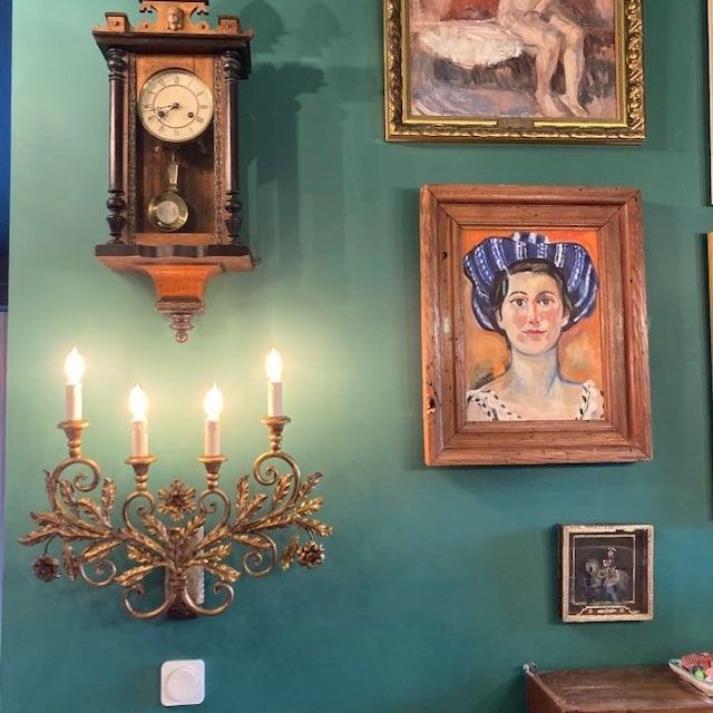 a wall with pictures and paintings on it, including a chandelier in the corner