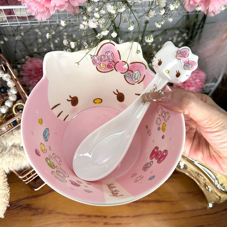 a pink hello kitty bowl and spoon set on a table with flowers in the background