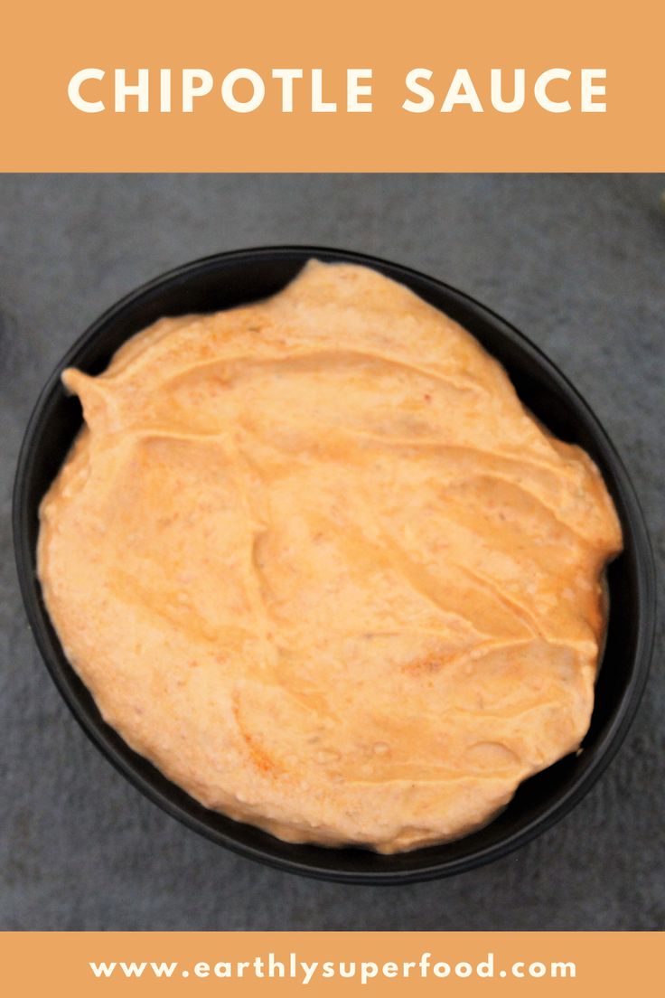 a black bowl filled with sauce sitting on top of a gray counter next to peppers