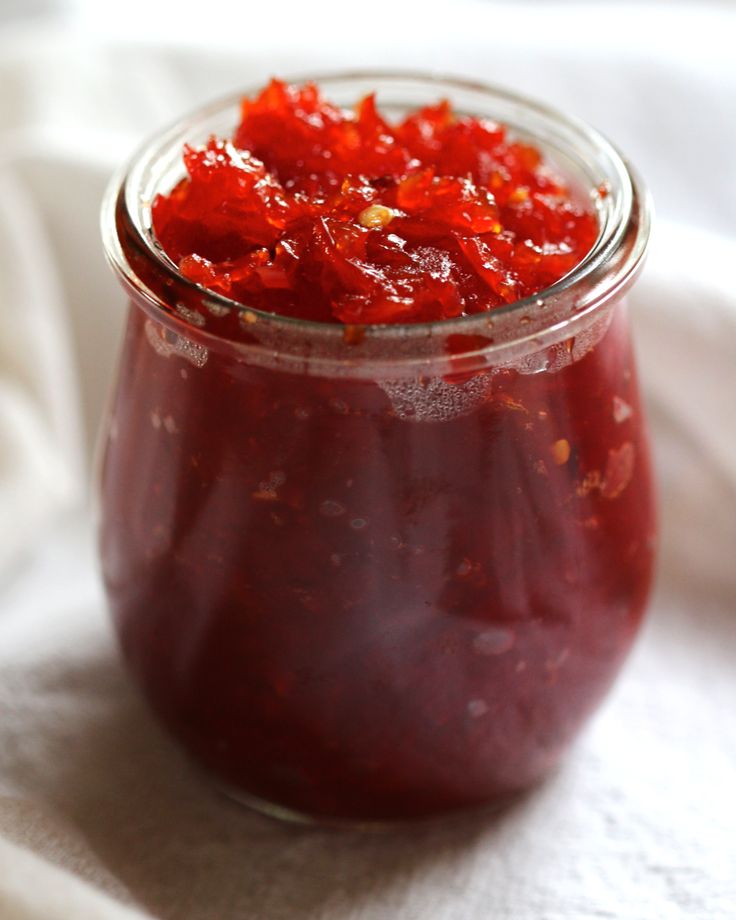 a glass jar filled with red pickles sitting on top of a white table cloth