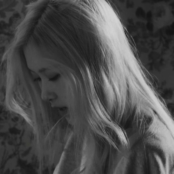 black and white photograph of a woman looking down at her cell phone while standing in front of a floral wall